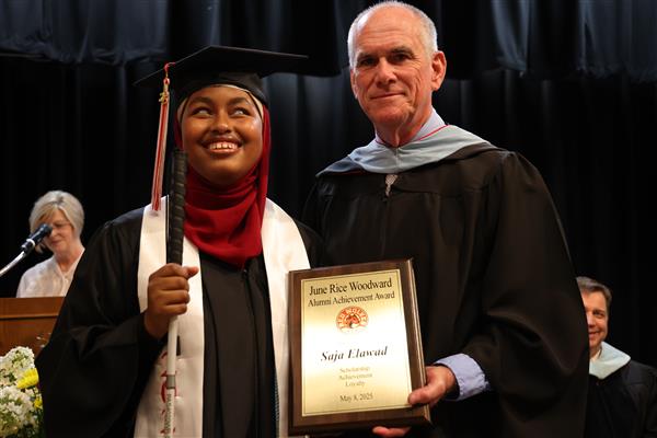 A graduate from the Alabama School of Alabama receiving a June Rise Woodward Alumni Achievement Award. She wears a black cap and gown, a red hijab,  and a white stole. She poses, smiling, with the principal from the Alabama School for the Blind who wears a black ceremonial robe and a light blue hood